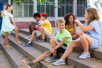 Children talking together while sitting on stairs outdoors. Youngsters chatting during summer day.