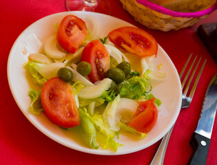 Traditional Valencian salad with lettuce leaves, sliced tomatoes, onions and olives, seasoned with olive oil