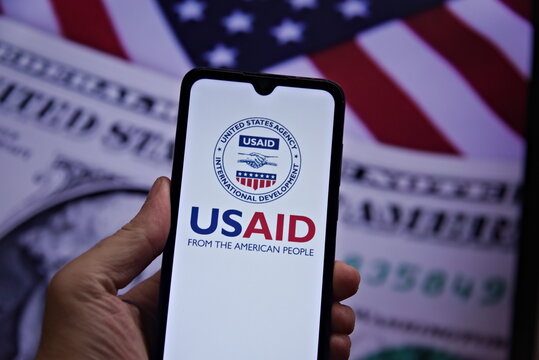 Cell phone with United States Agency for International Development (USAID) seal in the foreground and US dollar in the background