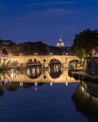 Obraz premium Reflection of a historic arched bridge crossing the Tiber River with Vatican City in the background. Ponte Umberto I