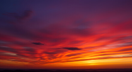 Obraz premium Vivid twilight sky transitioning from deep purple to fiery red with scattered cloud streaks