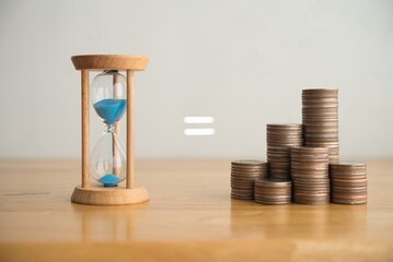 Hourglass equal to heap stack coins on wooden table with white wall background. Time is money aphorism. Financial and time management concept.