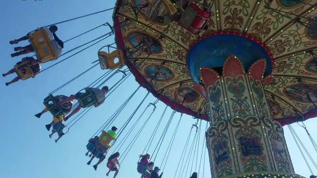 Young and old people riding a carnival chair ride at an amusement park or fair in the summer. 