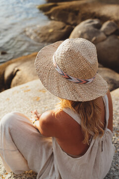 Blond woman wearing straw hat meditating near the sea