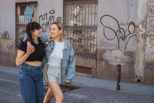Two young women holding hands are walking on the street and smiling