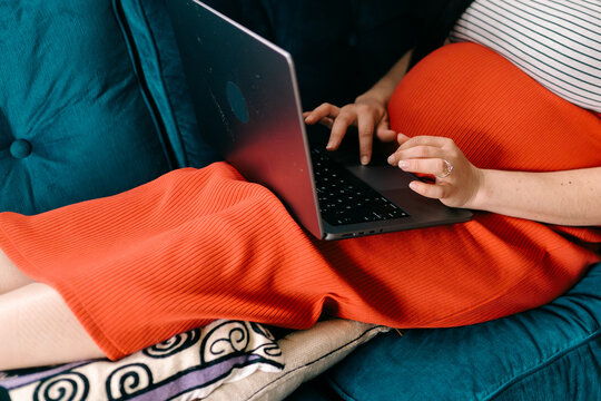 pregnant woman sitting with feet up on sofa  scrolling on  laptop