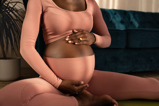 Pregnant woman touching belly while exercising in sunlight at home