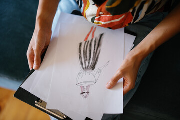Cropped female designer holding paper with sketch of clothes model