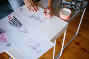 Partial designer drawing sketches of clothes on papers with pencil