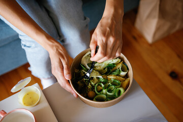Top view of cropped woman mixing natural tasty salad in bowl at table