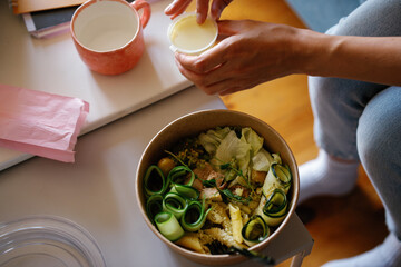 Top view of cropped woman opening sauce for salad in bowl at table