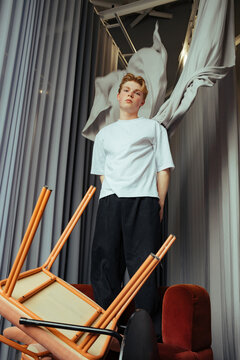 Model stands amidst overturned furniture in modern interior design