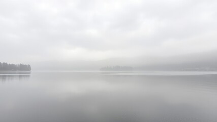 Fototapeta premium Overcast sky and misty atmosphere on a still lake at midday in the Italian countryside, serene, overcast