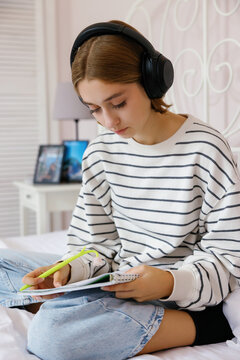 Young blonde female school student watching notebook on bed at home