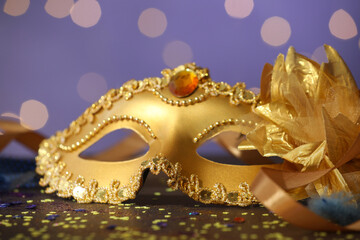 Beautiful carnival mask, ribbons and confetti on color background with blurred lights, closeup