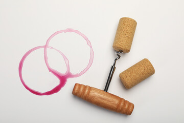 Corkscrew, cork and red wine stains on white background, top view