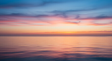 Obraz premium Gentle pink and orange hues reflecting off a calm evening sky over the ocean horizon