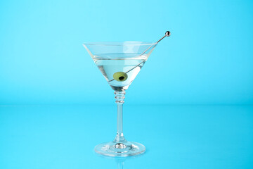 Martini cocktail with olive in glass on light blue background