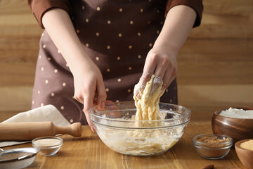 Woman kneading dough for cinnamon rolls at wooden table, closeup