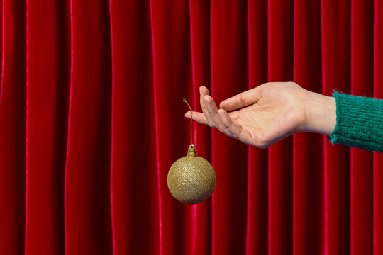 A hand holding a golden Christmas ornament  against a vibrant re