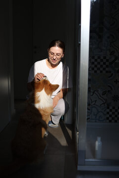 Smiling woman gives something to her dog squatting in bathroom