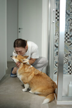 Woman kissing and cuddling corgi in bathroom before bathing it