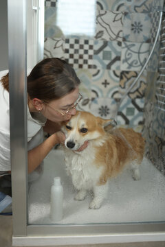 View through glass of woman kissing dog while washing it in shower