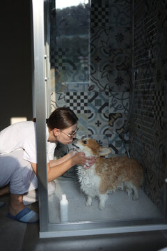 Woman kissing her corgi while washing its fur in shower cabin
