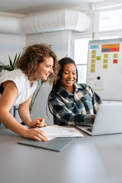 Two businesswomen collaborating on laptop in coworking space