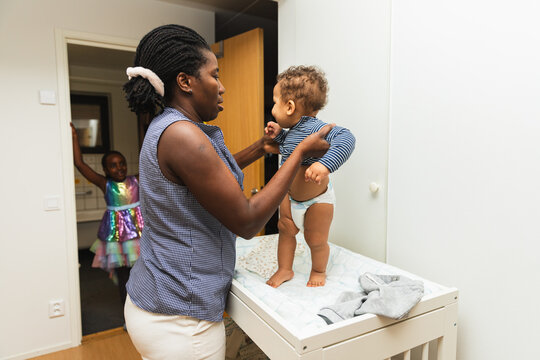 Mother Changing Baby's Clothes on Changing Table in Home Corridor