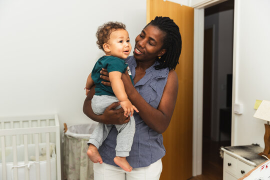Mother Holding Baby, Smiling at Camera in Bedroom