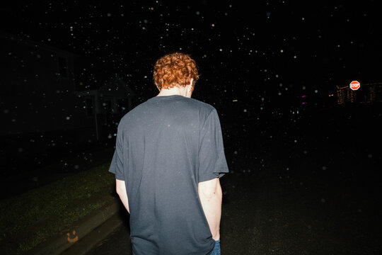 Pale young man in T-shirt with red hair walking in snow at night