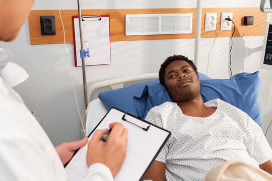 Doctor taking notes about a black patient lying in hospital bed