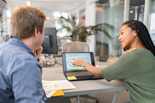 Coworkers discussing statistics on laptop in modern office