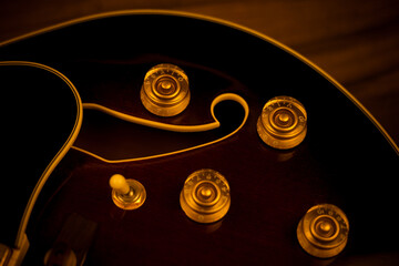 Close-up of guitar body with knobs and f-hole design, warm lighting.