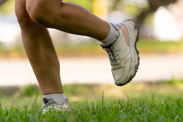 Woman running on grass in park wearing white sneakers, exercising outdoors