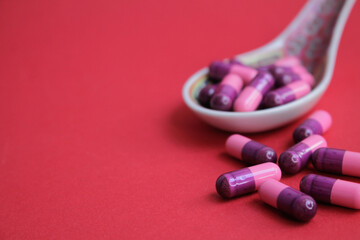 Capsulas de color rosa sobre una cuchara de porcelana y con un fondo rojo.