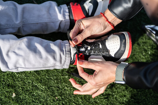 Woman tying shoelaces of child's sneakers on artificial grass