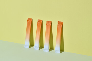 Three vibrant orange citrus stick packs are displayed against a yellow