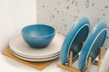 minimalist tableware in neutral tones, arranged on a white countertop against a light-colored wall with a subtle terrazzo pattern