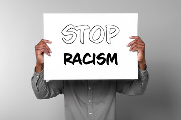 Man holding paper with text Stop Racism on grey background, closeup