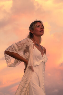 Woman in white dress poses against a vibrant sunset sky