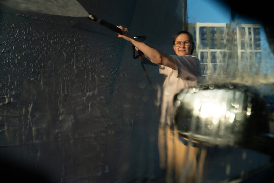 Woman Washing Car with Pressure Washer Through Wet Glass