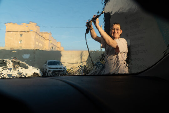 View Through Wet Glass of Woman Washing Car