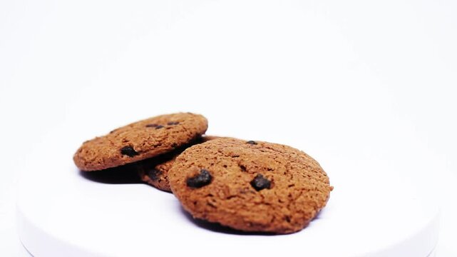 shot of a hand reaching for a chocolate chip cookie from a plate. Warm lighting enhances the golden-brown texture. A tempting, delicious treat ready to be enjoyed