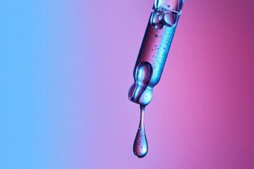 Clear glass pipette with a drop of cosmetic product falling down. 