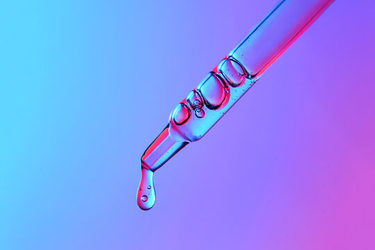 Clear glass pipette with a drop of cosmetic product falling down. 