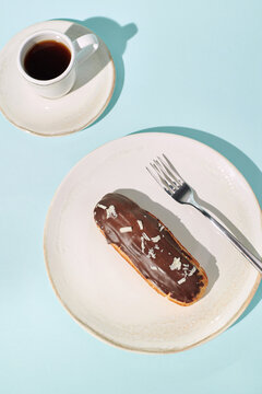 Enjoying coffee and chocolate eclair on a bright turquoise table