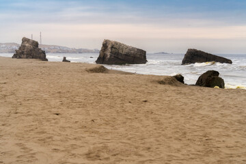 Rocks emerging from the sand on a beach with city in background