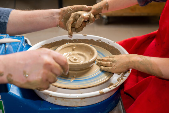 Master and a child make a clay plate on a potter's wheel